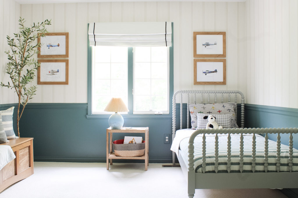 An airplane themed boy's bedroom design. Walls are painted sherwin william's riverway. There are grey Jenny Lind bed's. A tan stripe wallpape is on the walls. 