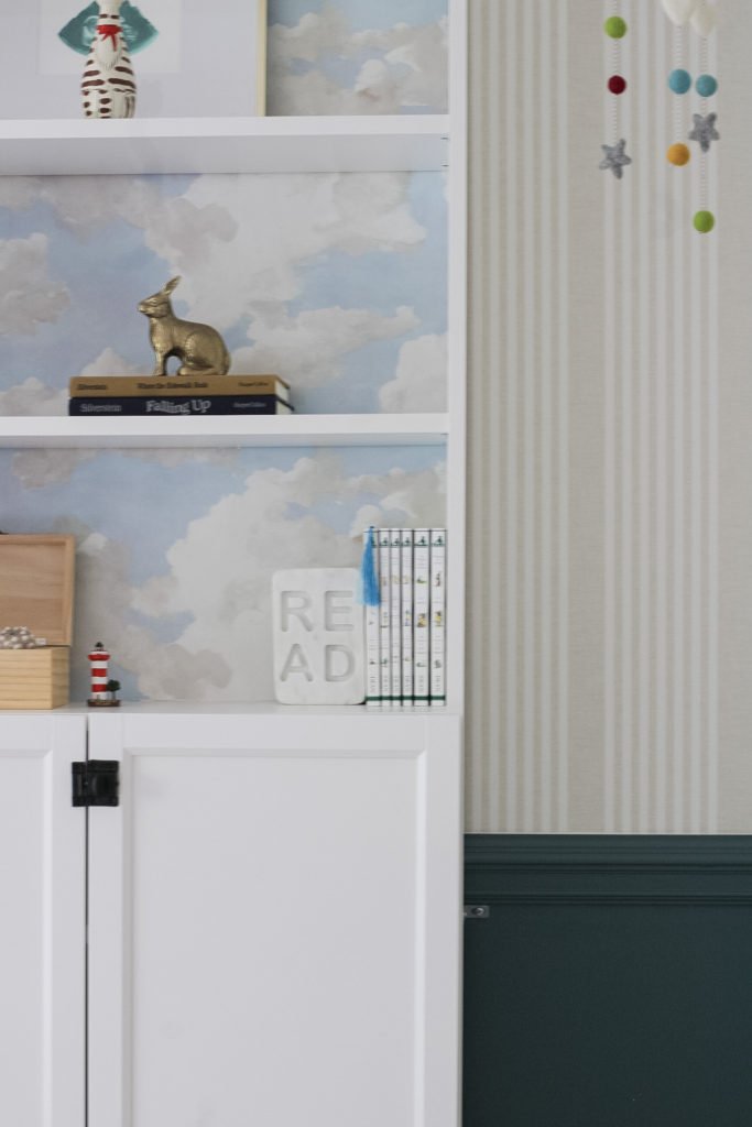 An Ikea billy bookcase that has blue cloud wallpapaer in the background. The walls are painted sherwin william's riverway on the lower half and above the chair rail is a linen stripe wallpaper. 