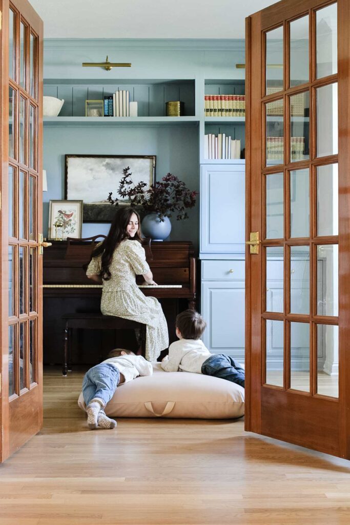 piano surrounded by cabinets painted in Sherwin William Debonair, blue with mother playing piano and little boys lounging on cushion on floor listening