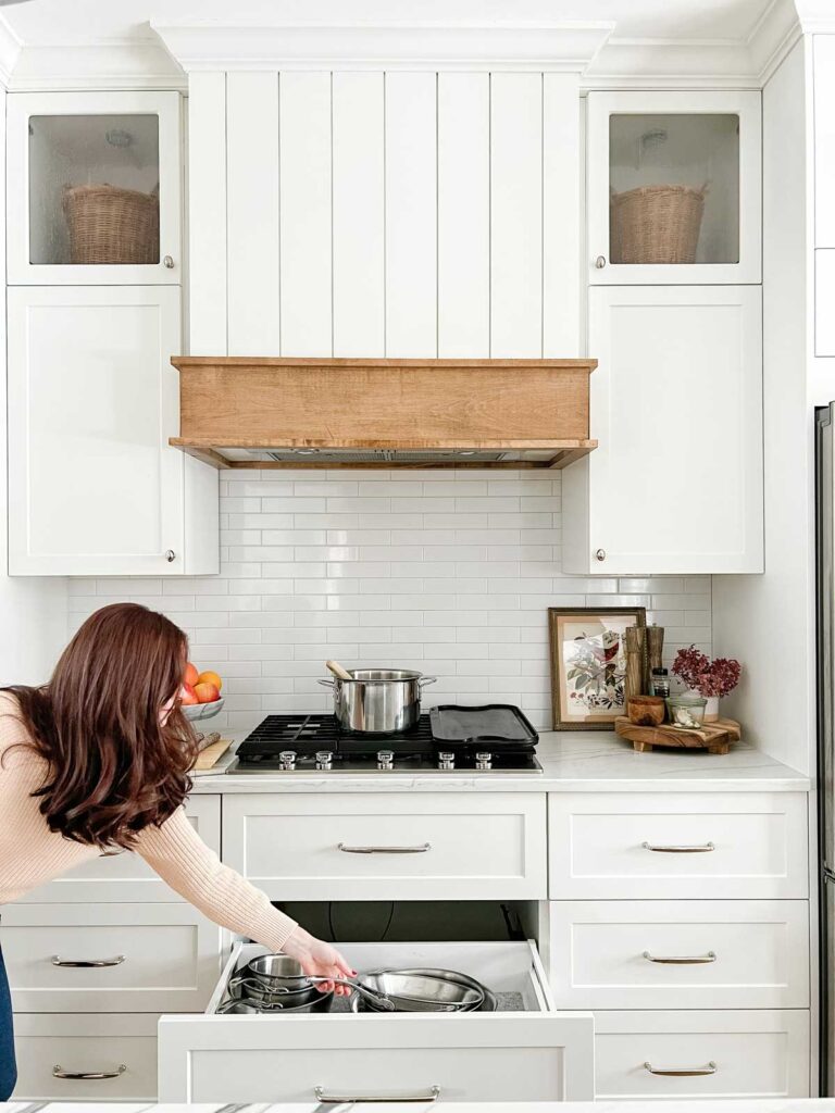 ikea kitchen with white cabinets and drawers. Showing the cabinets around gas cooktop with a drawer open showing pan storage.