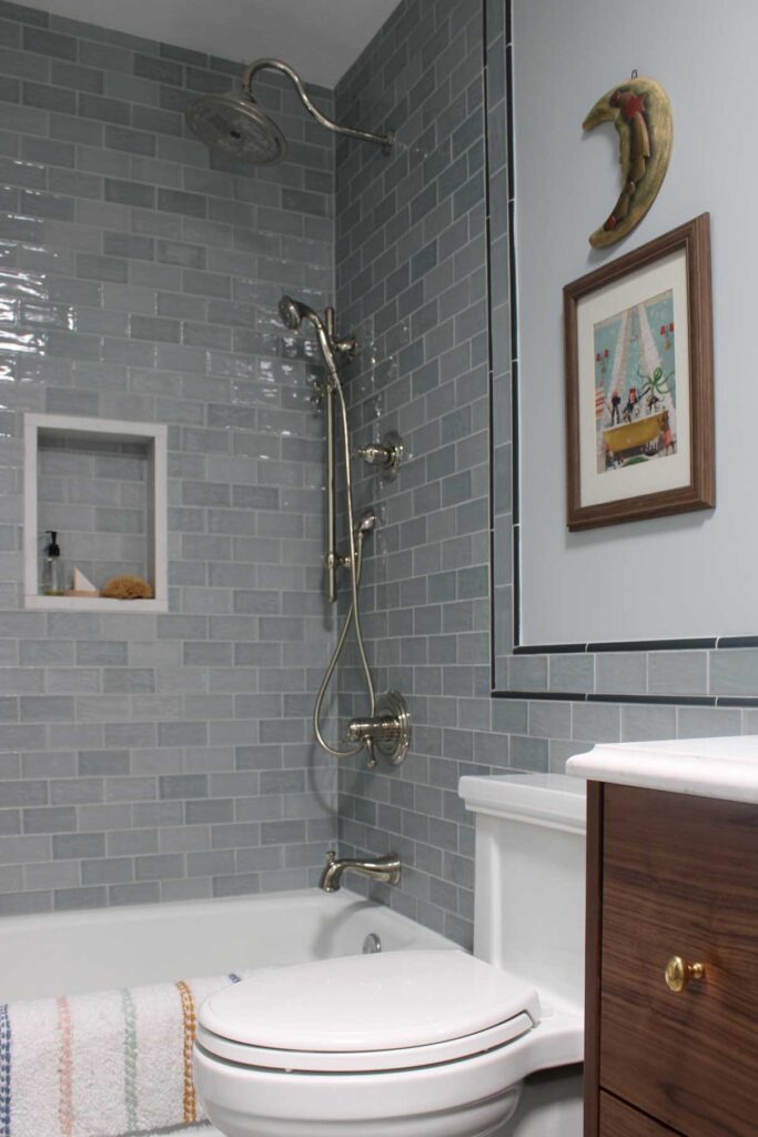 A boys bathroom with blue subway tile. A shower niche is framed in quartz. Polished nickel shower head, tub spout, and hand sprayer. 