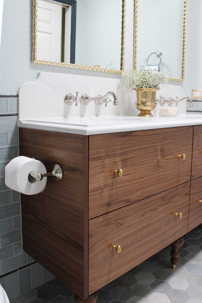 Walnut vanity made from an Ikea godmorgon hack. Brass mirrors hang over the vanity. Wallmount faucets are in a vadara sterling light quartz backsplash. Blue wall and floor tile surround the vanity.