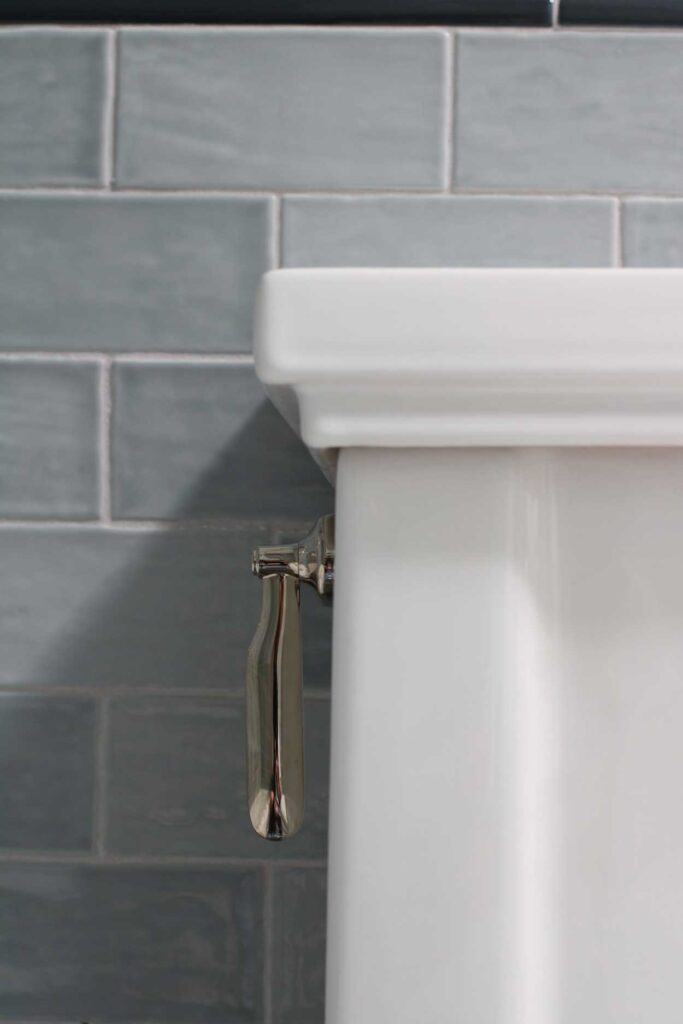 Bedrosians Marin blue subway tile with warm gray grout on bathroom walls. A kohler polished nickel toilet lever on a kohler tresham one piece toilet. 