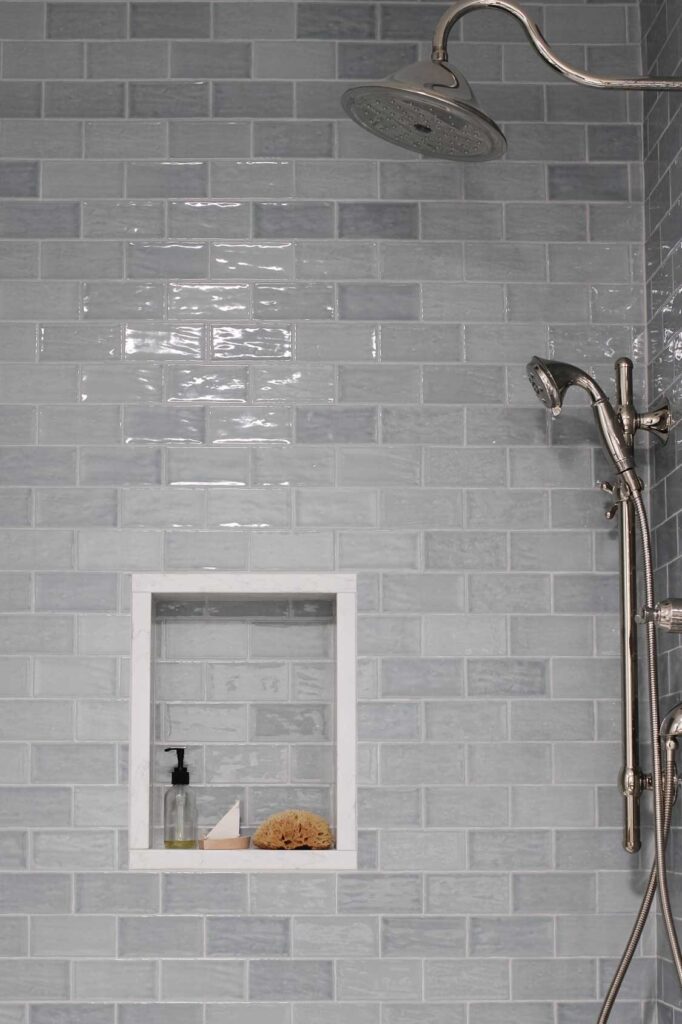 Bedrosians Marin blue subway tile with warm gray grout on shower walls. A vadara quartz sterling light shower niche. Polished nickel bath and shower fixtures. 