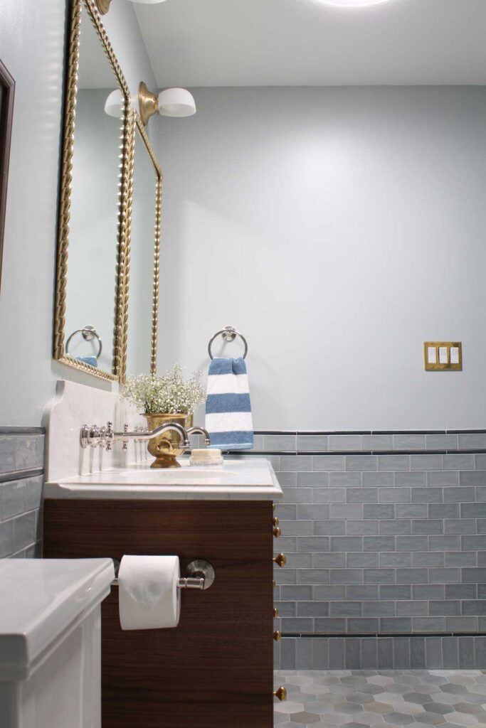 Walnut vanity made from an Ikea godmorgon hack. Brass mirrors hang over the vanity. Wallmount faucets are in a vadara sterling light quartz backsplash. A 1/2 wall of blue subway tile with a border detail. 