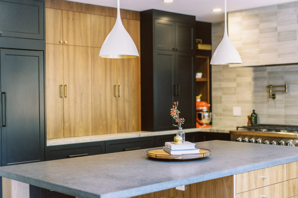 kitchen with black cabinets and walnut cabinets. white pendants hang over the island. 